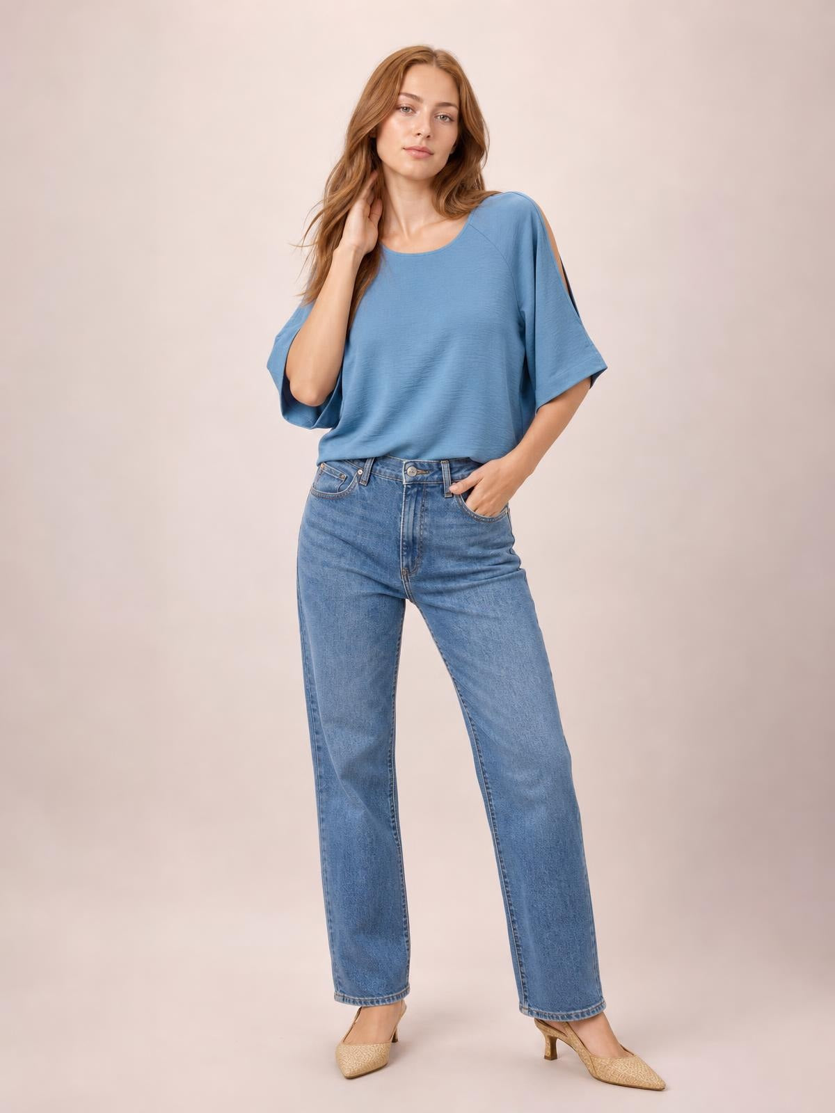 Model poses in a blue textured round neck top with split cold-shoulder half sleeves and a relaxed long silhouette, paired with jeans.