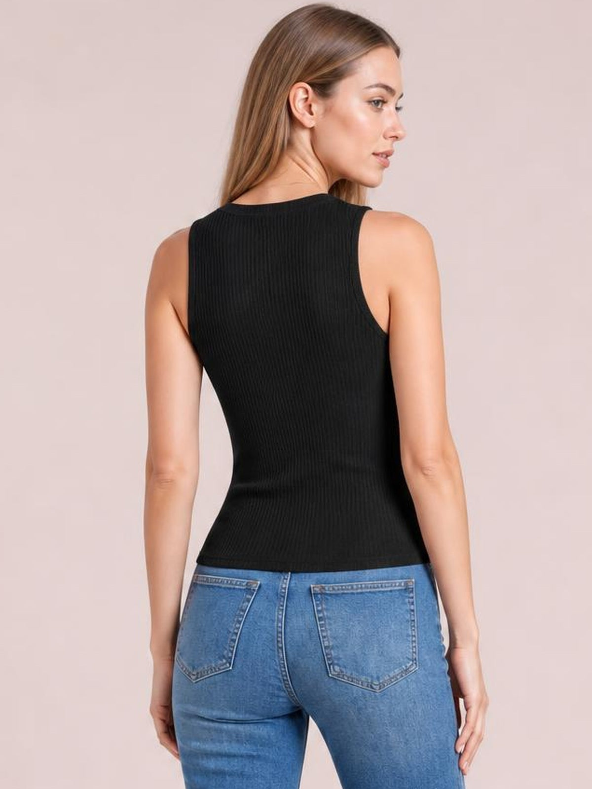 A model poses in a fitted black textured round neck tank, showing its sleeveless cut, vertical ribbed construction, and curved hem with blue jeans.