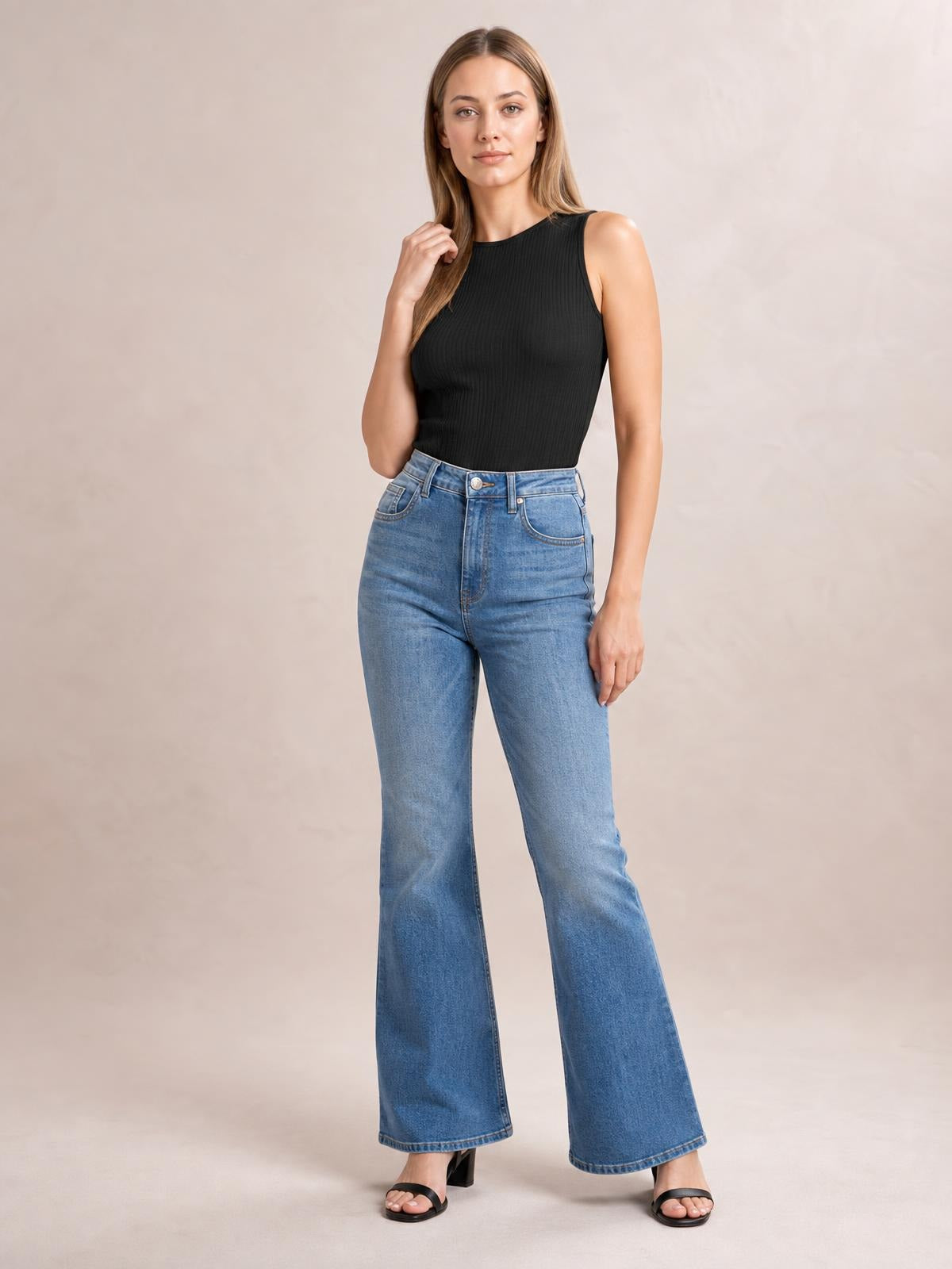 A model poses in a black textured round neck tank with a sleeveless cut, fitted silhouette, and subtle vertical ribbed construction, paired with wide-leg jeans.