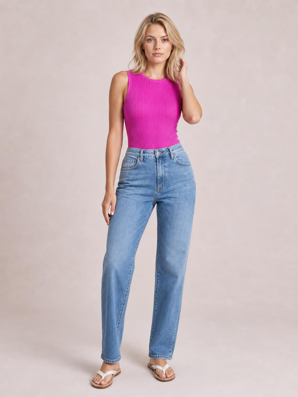 Model poses in a bright pink textured round neck tank with a fitted sleeveless silhouette, paired with high-rise light blue straight-leg jeans.