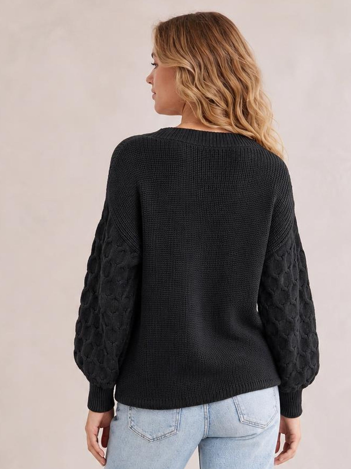 A model wears a black textured-sleeve round-neck sweater with a relaxed silhouette, ribbed neckline, cuffs, and hem, shown from the back.