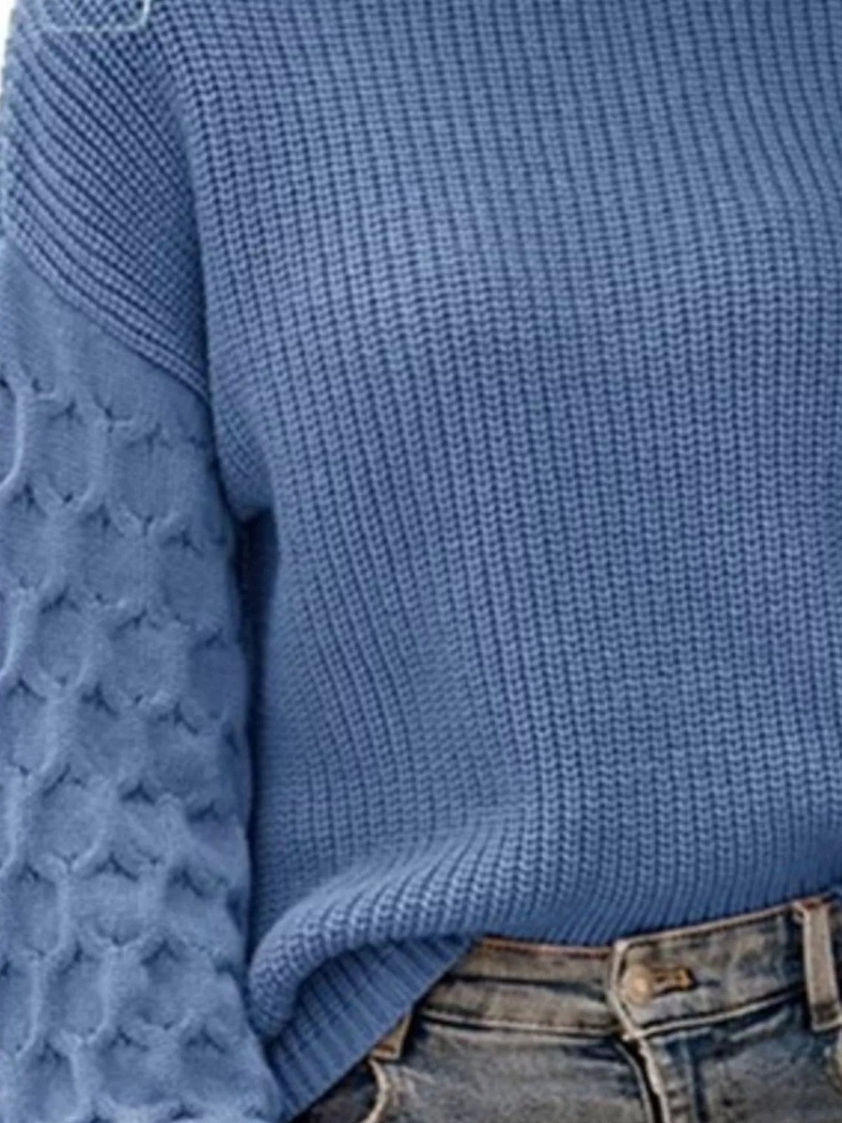 Close-up of a model wearing a blue textured sweater with a relaxed silhouette, ribbed sleeve and hem details, styled with faded jeans.