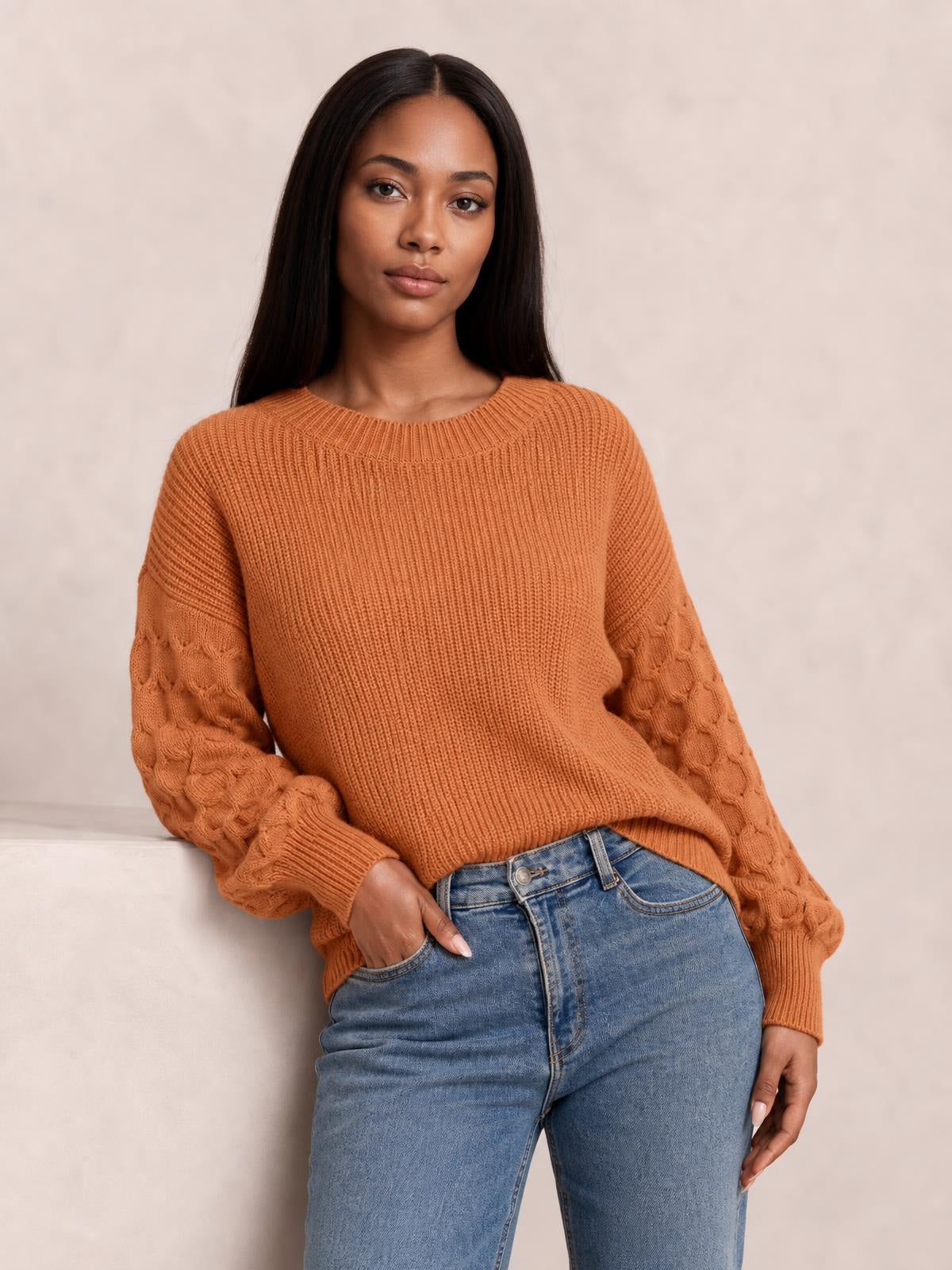 Model poses in a rust textured sleeve round neck sweater with ribbed trim, cable-knit sleeves, a relaxed silhouette, and stretch construction.