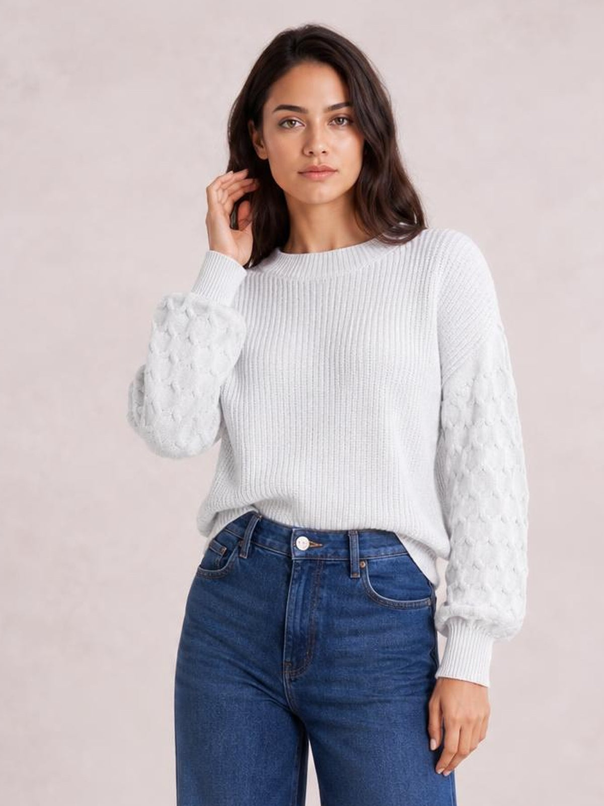 Model wearing a white textured sleeve round neck sweater with ribbed trim and a relaxed silhouette, posing with one hand touching her hair.