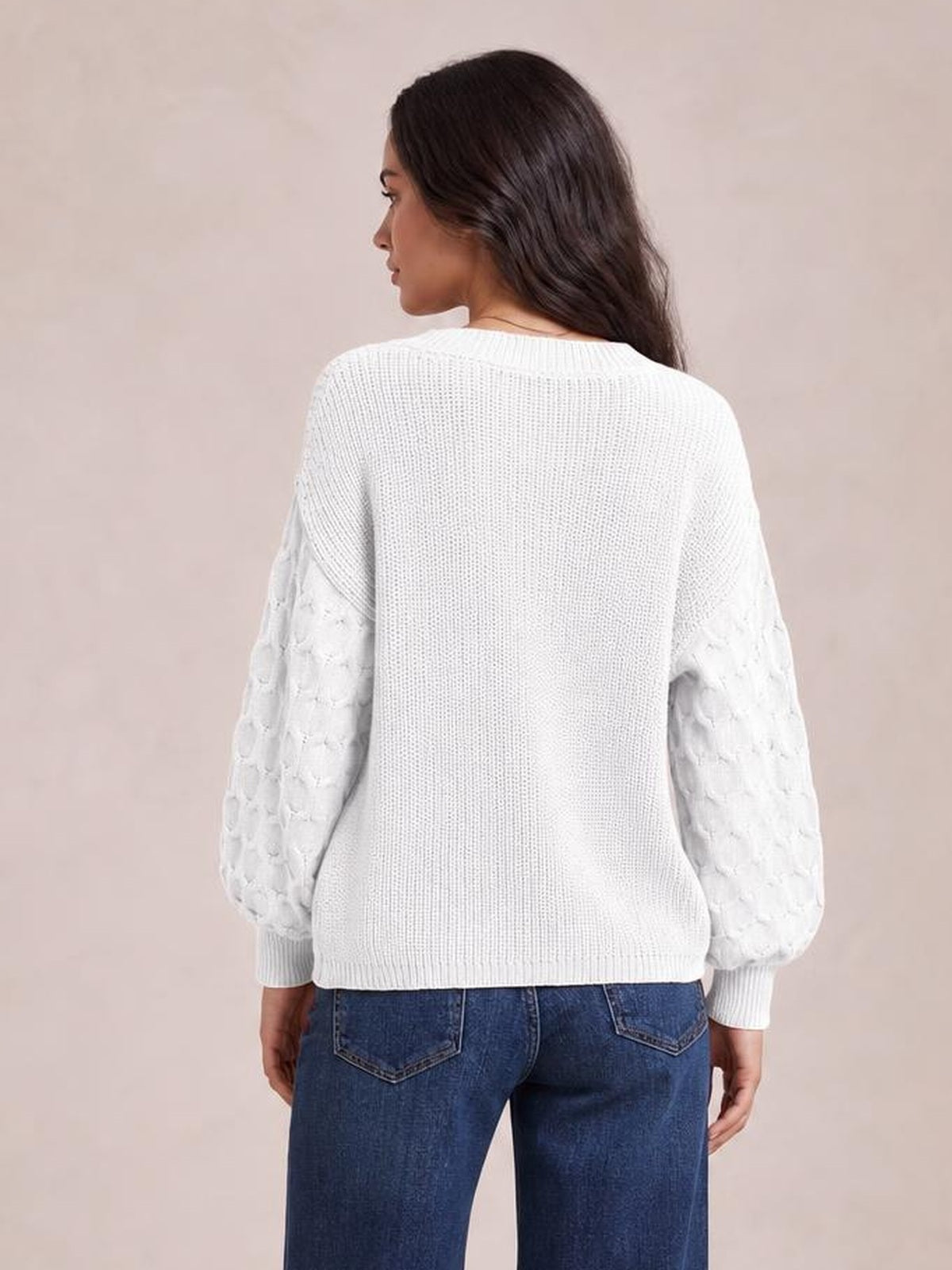 A model stands turned away in a white round-neck sweater with textured sleeves, ribbed cuffs and hem, and a relaxed, straight silhouette.