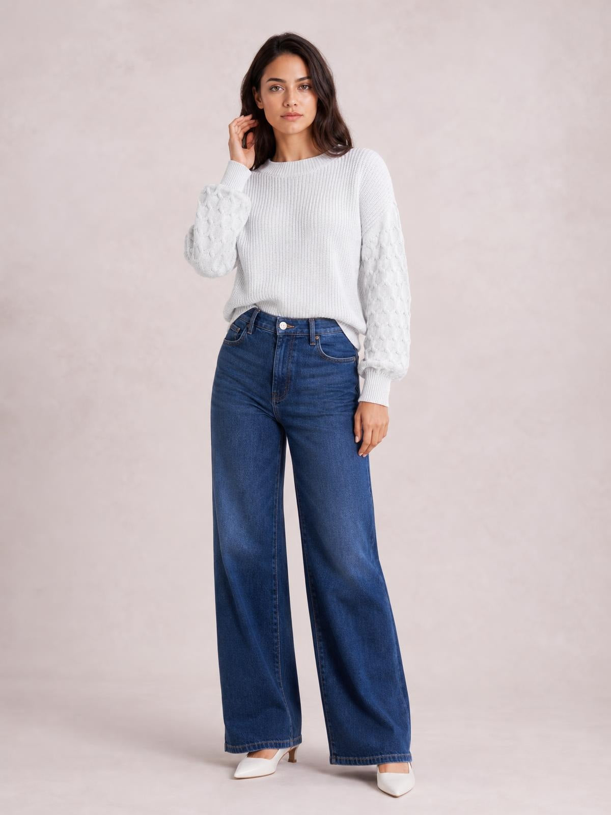 Model wearing a white textured sleeve round neck sweater with ribbed cuffs and hem, relaxed silhouette, and voluminous patterned sleeves while posing in wide-leg jeans.