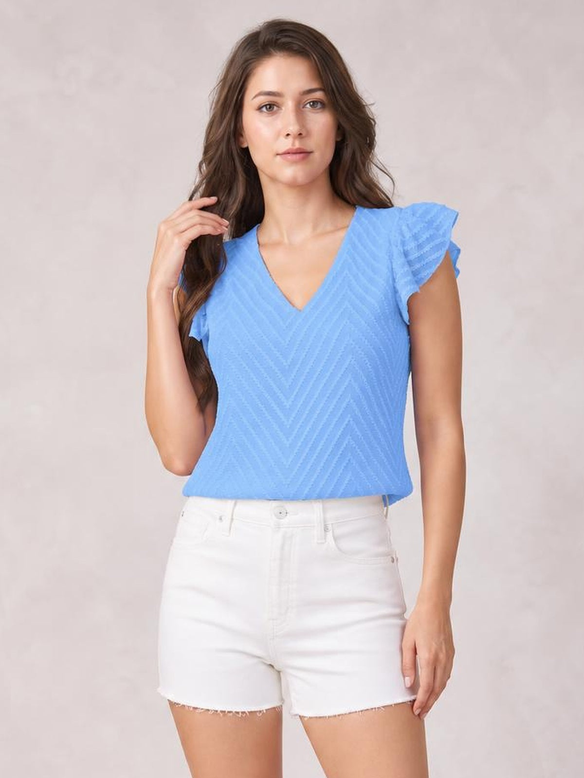 Model poses in a bright blue textured V-neck blouse with ruffled cap sleeves, a relaxed straight silhouette, and short sleeves.
