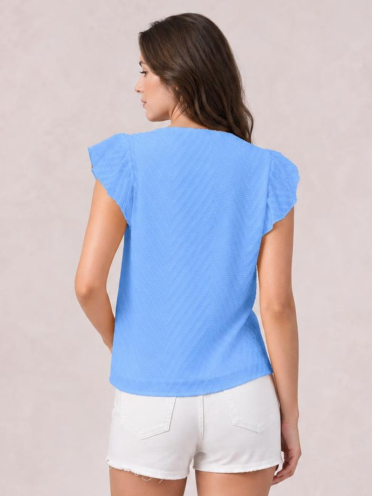 Model shown from behind wearing a bright blue textured cap-sleeve blouse with a relaxed straight silhouette, one hand resting at her hip.