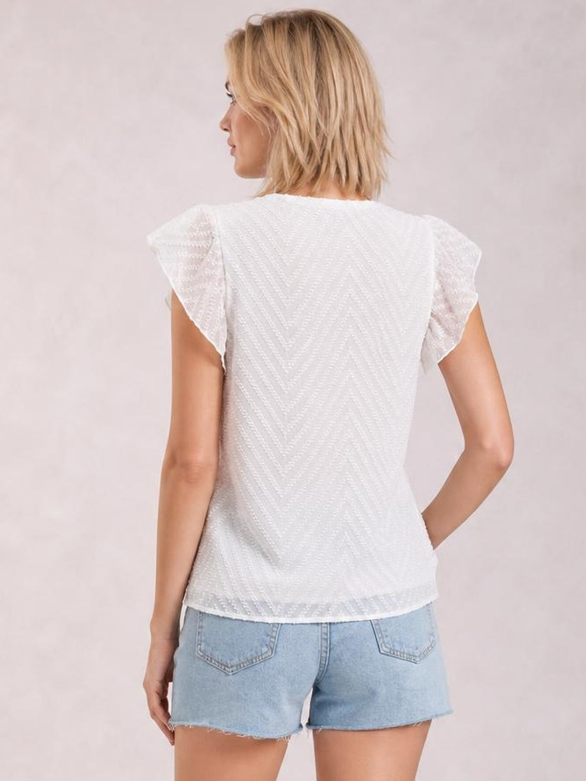 Model shown from behind wearing a white textured blouse with short cap sleeves, a relaxed straight silhouette, and a gently curved hem.