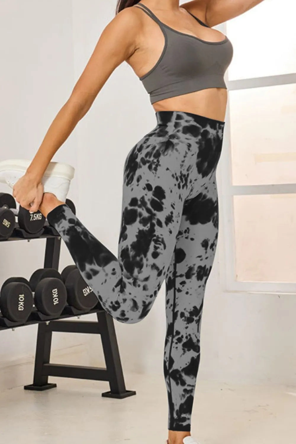 Model wearing gray and black tie-dye high-waist active leggings with a fitted full-length silhouette, lifting one bent leg in a stretching pose.