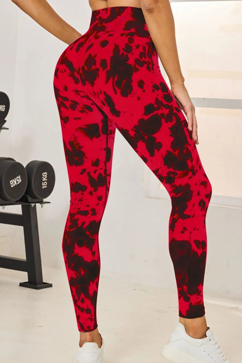 Model wearing red and black tie-dye high-waist active leggings with a fitted full-length silhouette, posed with one hand on her hip.