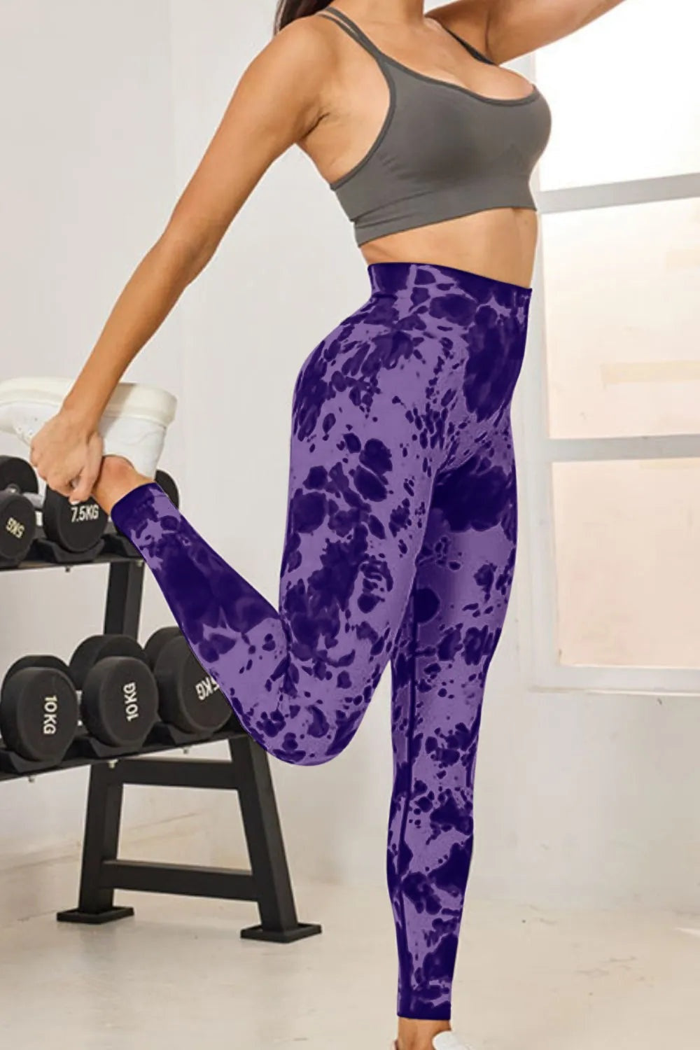 Model wearing purple tie-dye high-waist active leggings with a fitted full-length silhouette and stretch construction, balancing with one leg bent.
