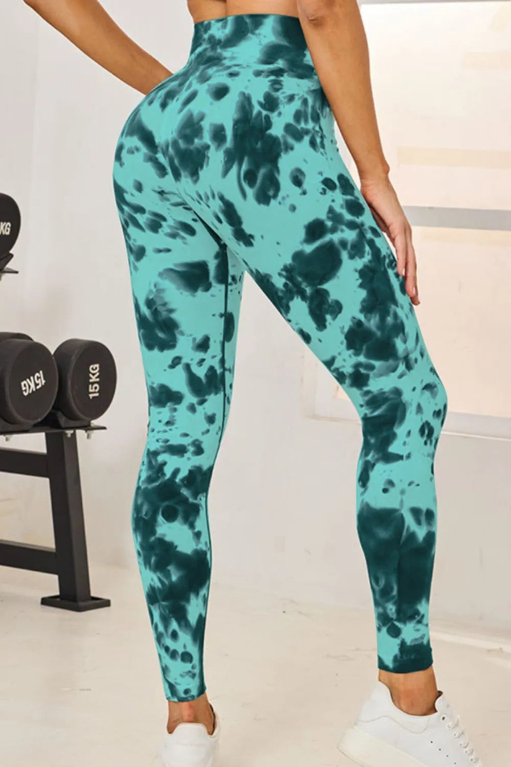 Model poses in turquoise and dark teal tie-dye high-waist active leggings with a fitted full-length silhouette and slight stretch.