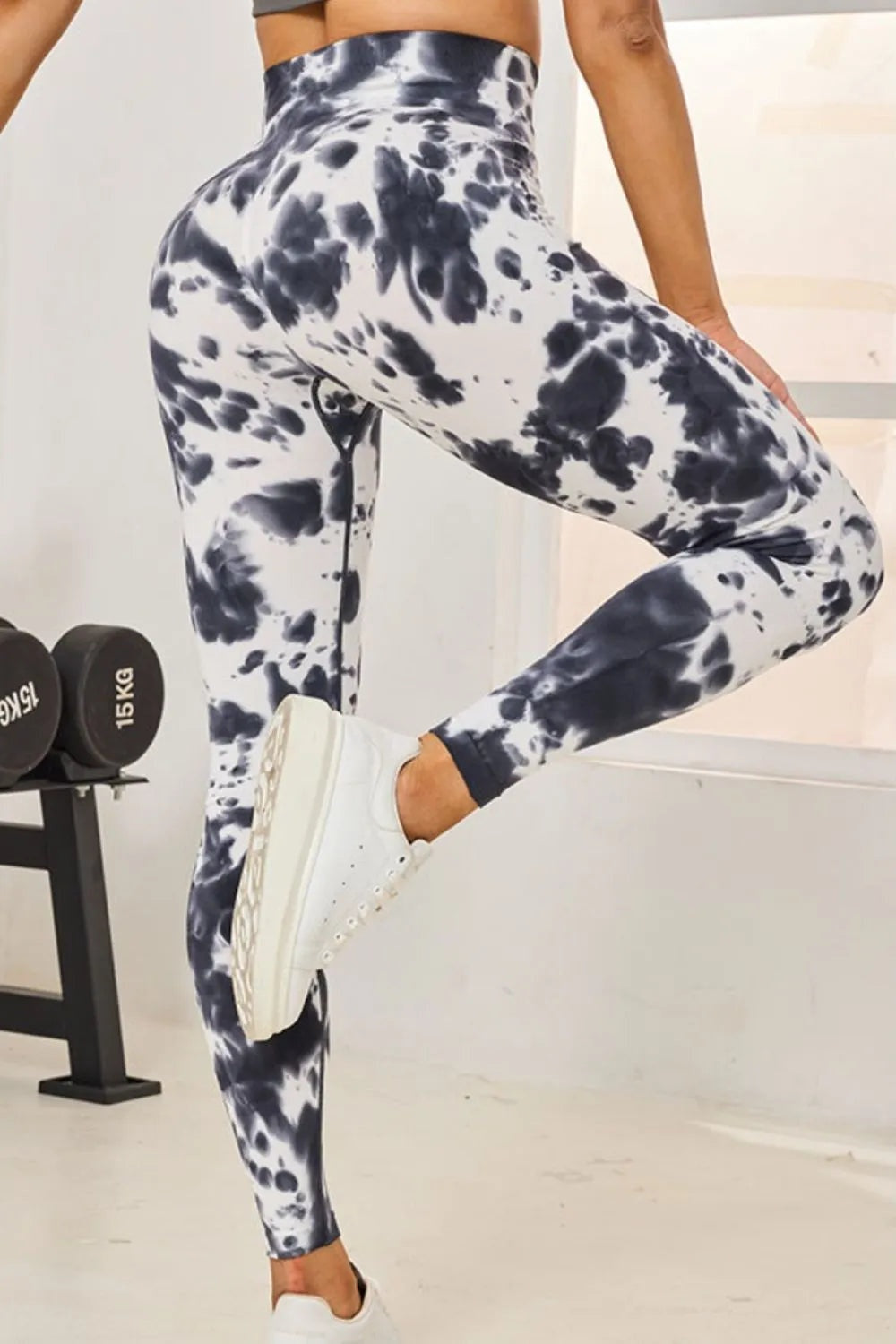 Model wearing high-waist tie-dye active leggings in a black-and-white pattern, with a fitted full-length silhouette and one bent leg.