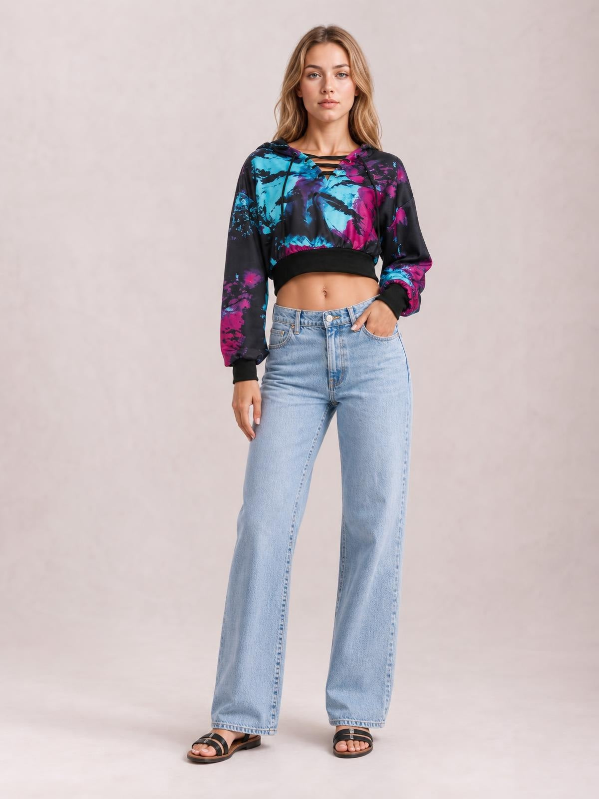 Model poses in a cropped tie-dye lace-up hoodie with black trim, long sleeves, and vibrant blue and magenta abstract coloring.