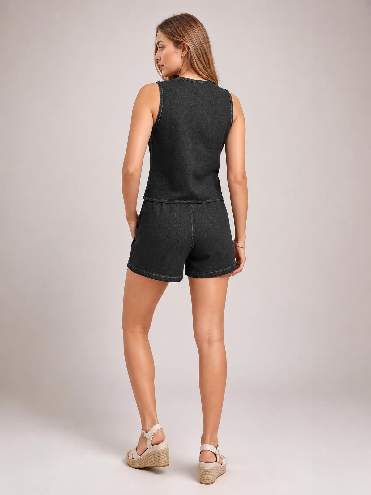 Model shown from behind in a black denim set with a sleeveless fitted top, defined seams, and matching high-waisted shorts in a relaxed standing pose.