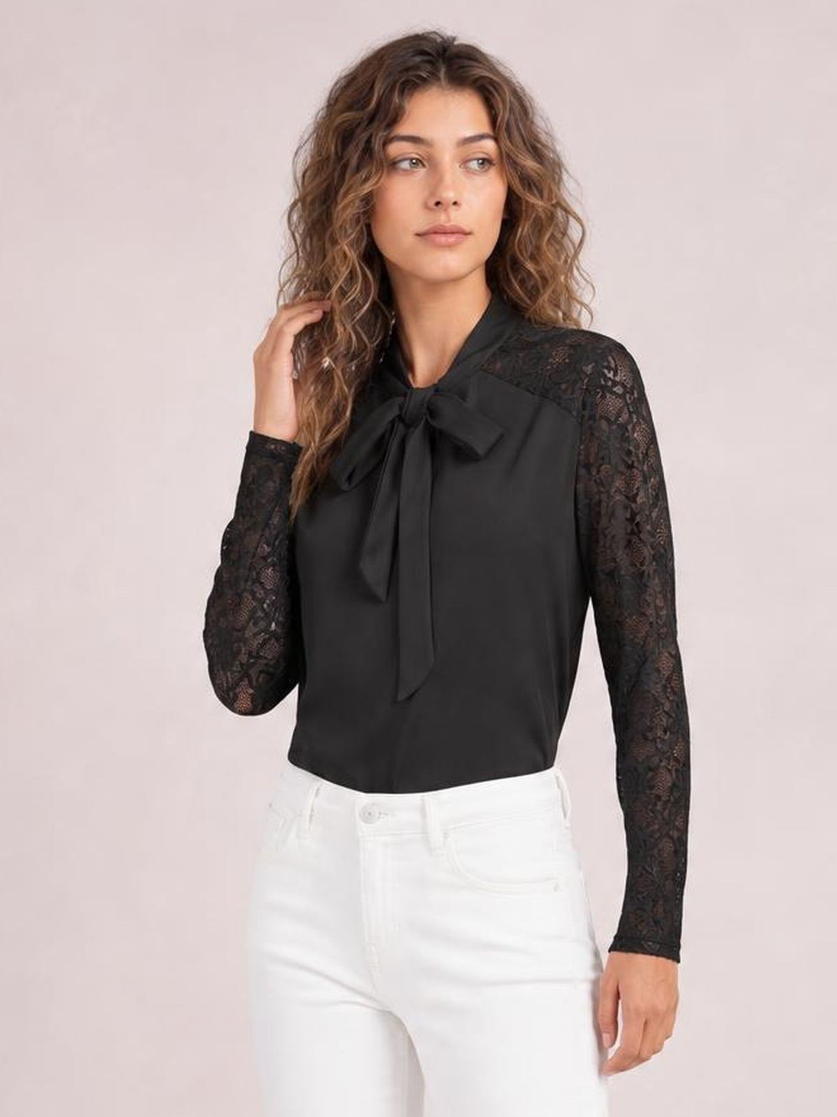 A model poses with one hand in her hair, wearing a black tie-neck blouse with a bow front, lace-spliced long sleeves, and a regular silhouette.