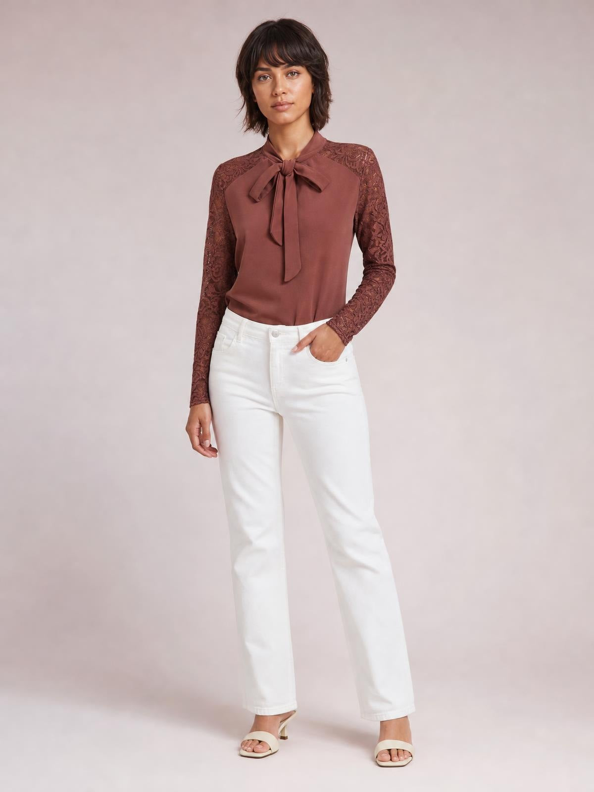 Model poses in a brown tie-neck top with a bow front, solid bodice, and spliced floral lace long sleeves in a regular silhouette.