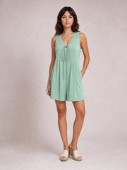 Model poses in a mint green sleeveless romper with a V-neck tie, pintuck detailing, loose silhouette, and relaxed shorts-length legs.