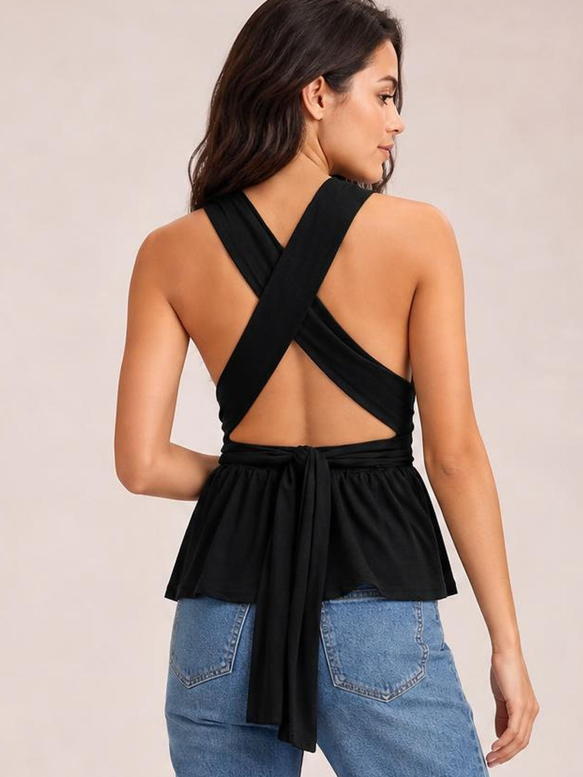 Model wears a black backless peplum top with a tied waist and crisscross back straps, shown from behind in a relaxed pose.