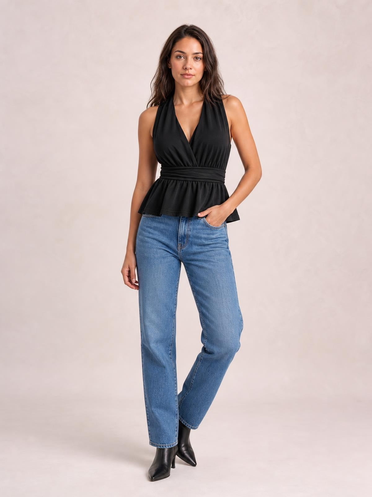 A model poses in a black sleeveless peplum top with a deep V-neck, gathered bust, wide tied waist, and flared hem over blue jeans.