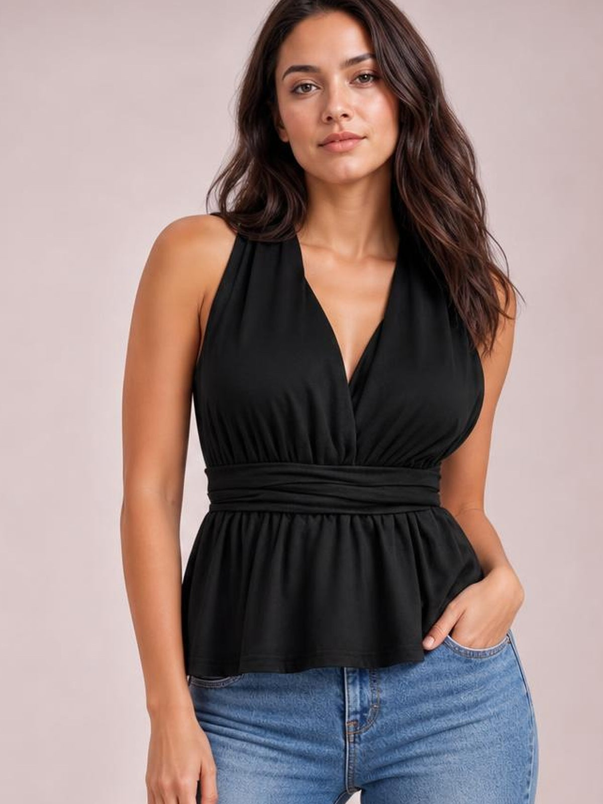 Model wearing a black backless peplum tank top with a V-neckline, gathered bust, tied waist detail, and flared hem.
