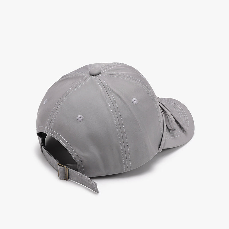 Gray cotton baseball cap with a tied bow near the curved brim, softly rounded paneled crown, neat topstitching, and an adjustable buckle back strap.