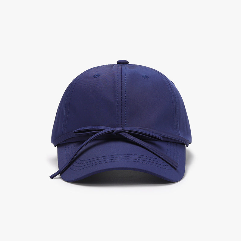 Navy cotton baseball cap with a softly rounded paneled crown, curved brim, neat topstitching, and a tied bow detail across the front.