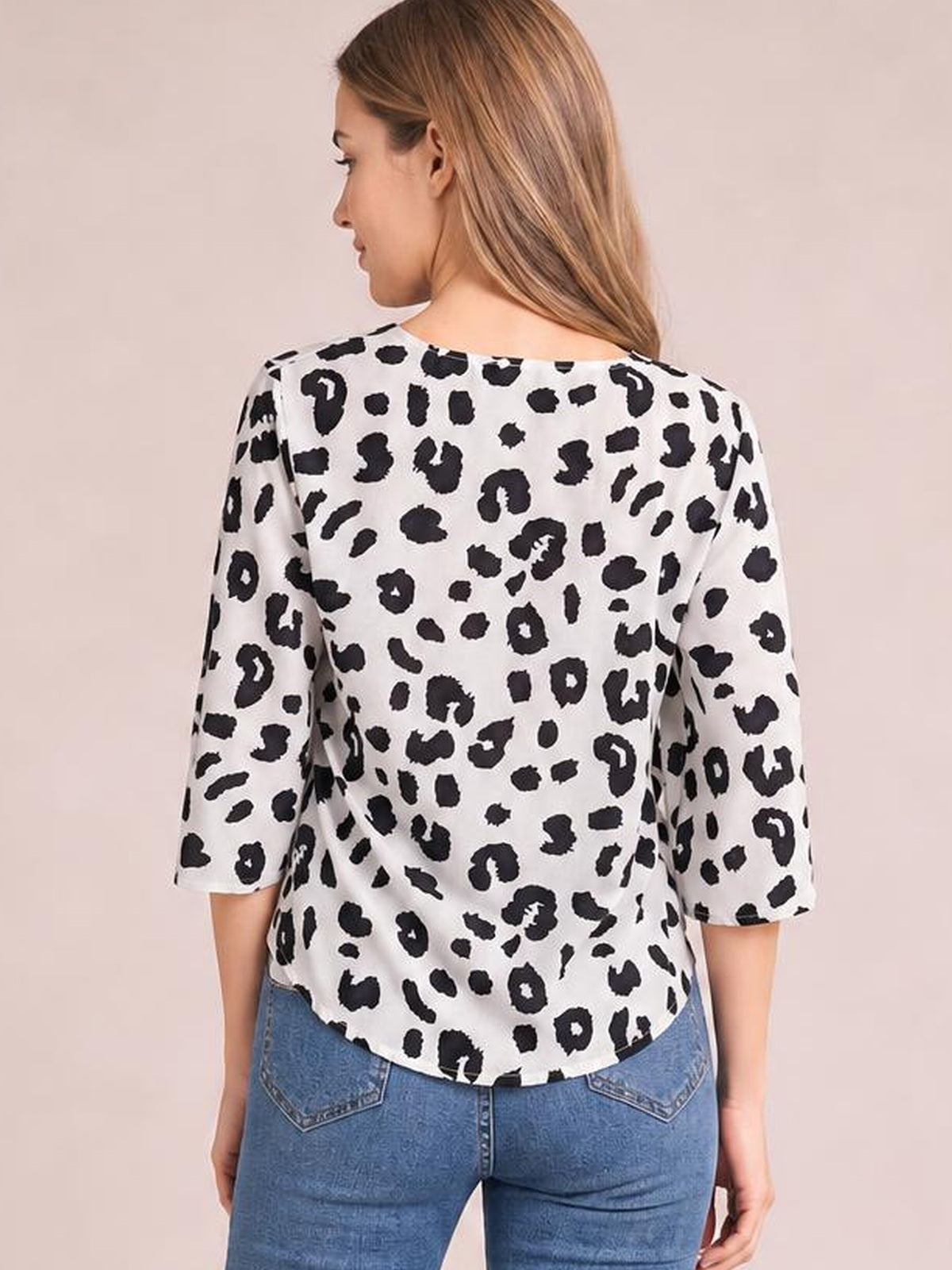 A woman stands in a back view wearing a white and black leopard-print blouse with three-quarter sleeves and a relaxed, curved-hem silhouette.