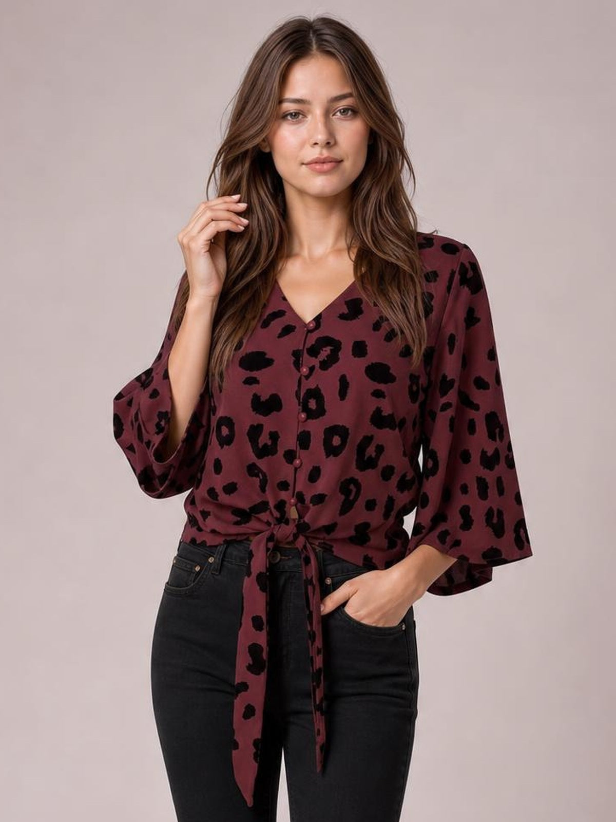 Model poses in a burgundy leopard-print V-neck blouse with button-up front, tied waist, relaxed silhouette, and flared three-quarter sleeves.