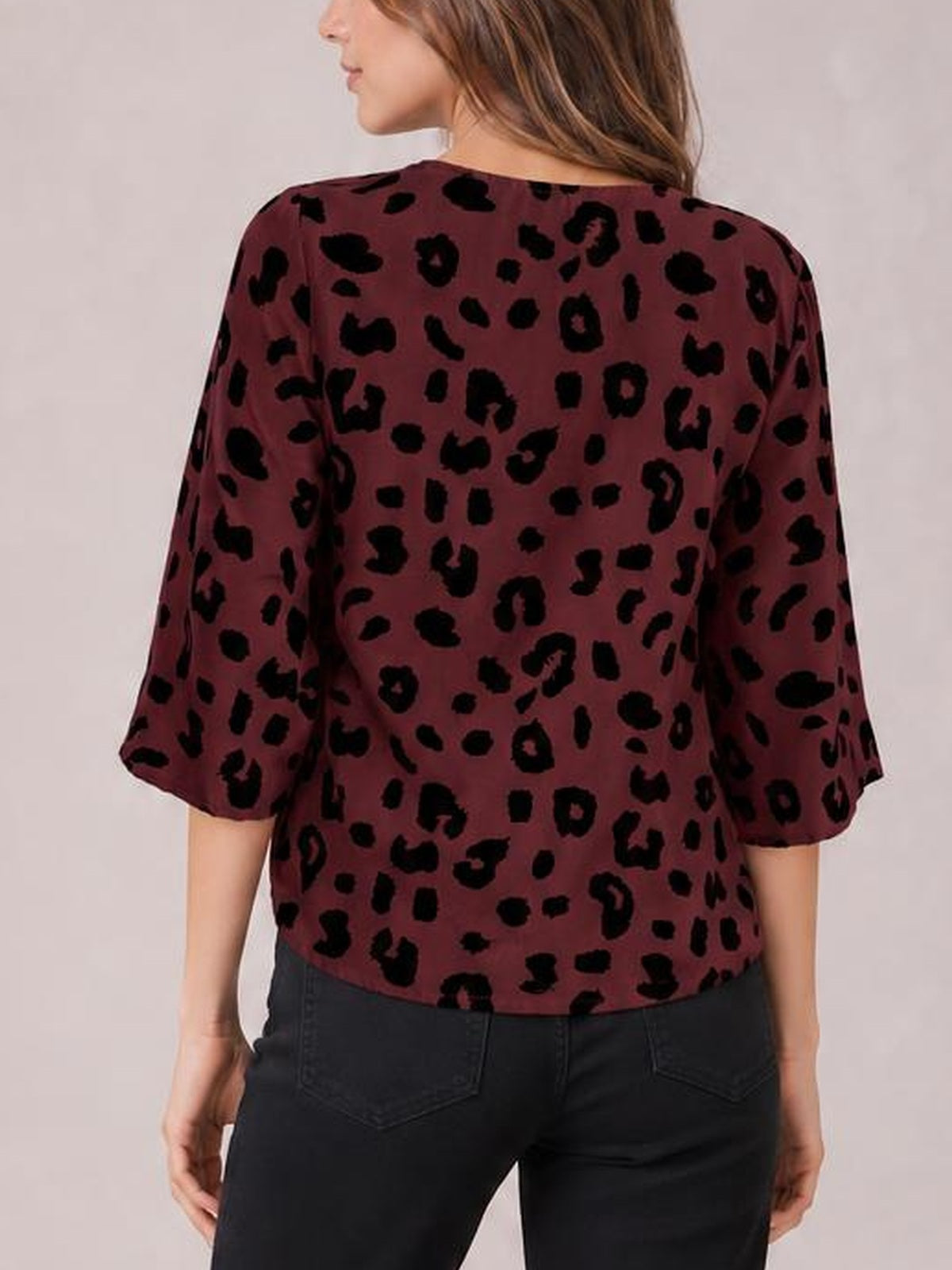 Back view of a model wearing a burgundy leopard print blouse with a relaxed silhouette and loose three-quarter sleeves, paired with black jeans.