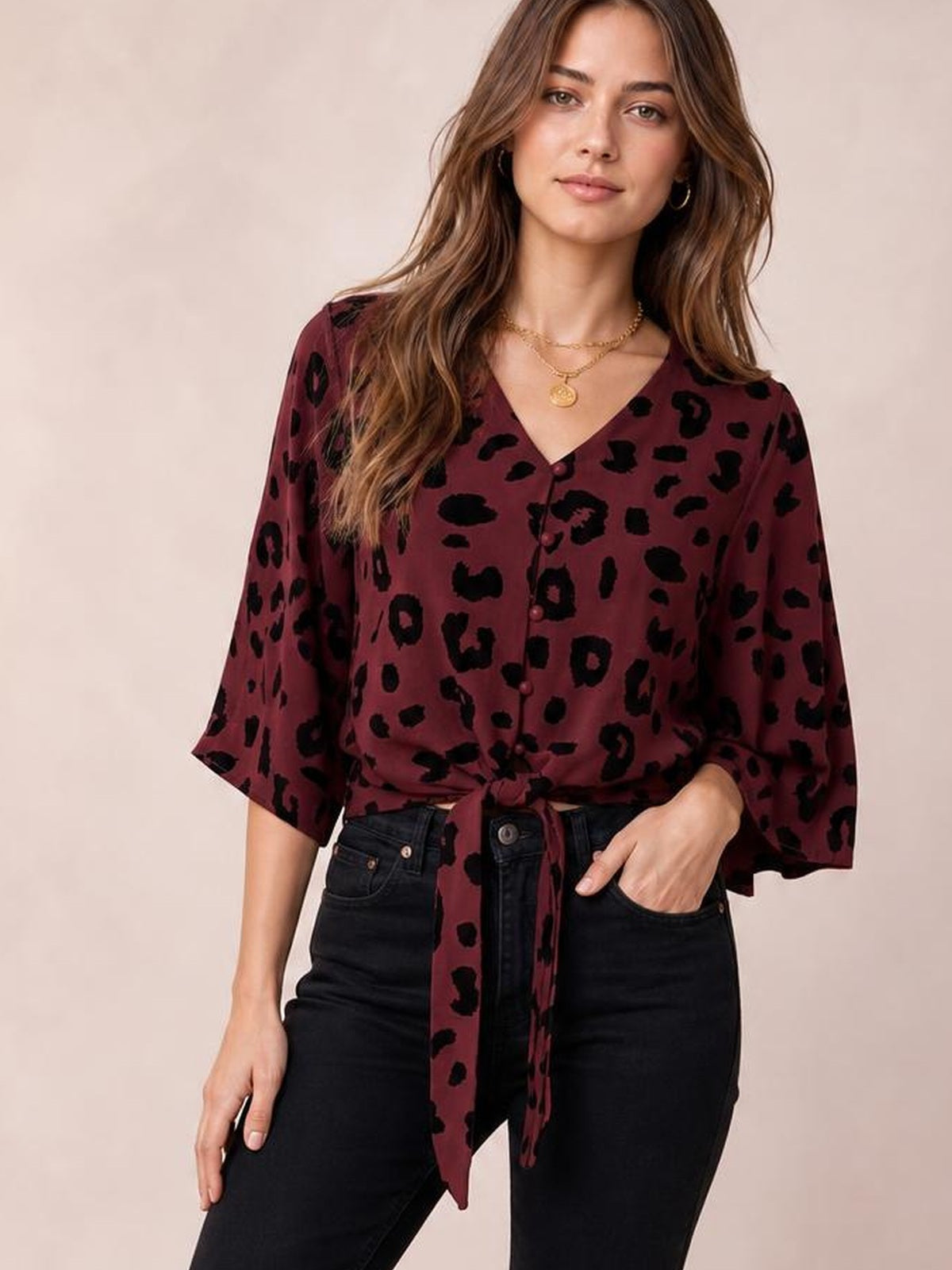 Model wearing a burgundy leopard-print V-neck blouse with front buttons, three-quarter sleeves, and a tied waist, paired with black jeans.