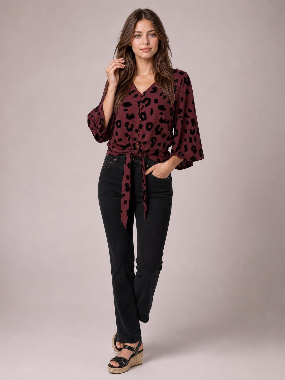 Model poses in a burgundy leopard-print blouse with a V-neck, button front, long sleeves, and a tied waist creating a relaxed silhouette.