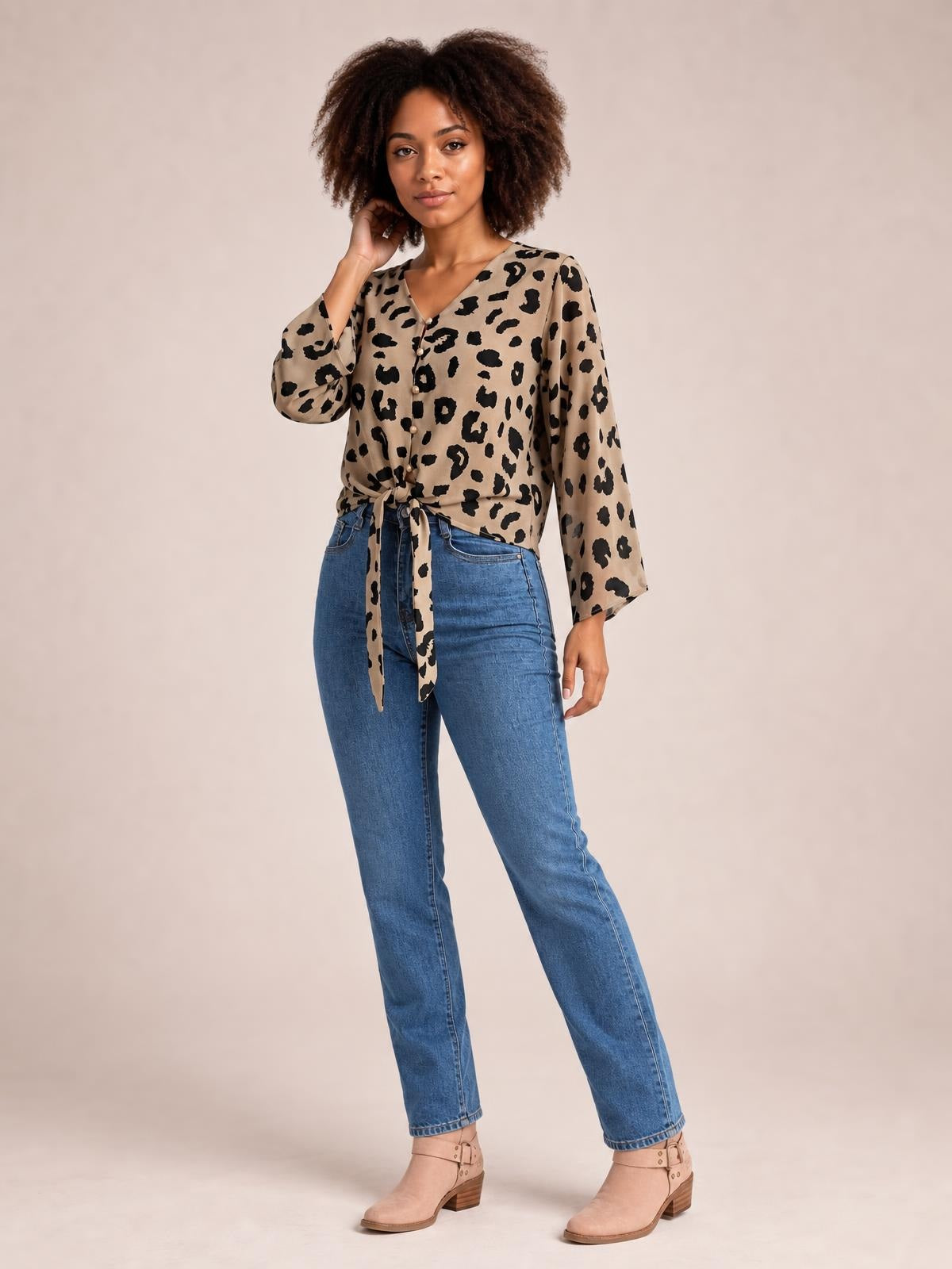 Model in a tan leopard-print blouse with a V-neck, button front, long sleeves, and tied waist, posing with one hand near her hair.