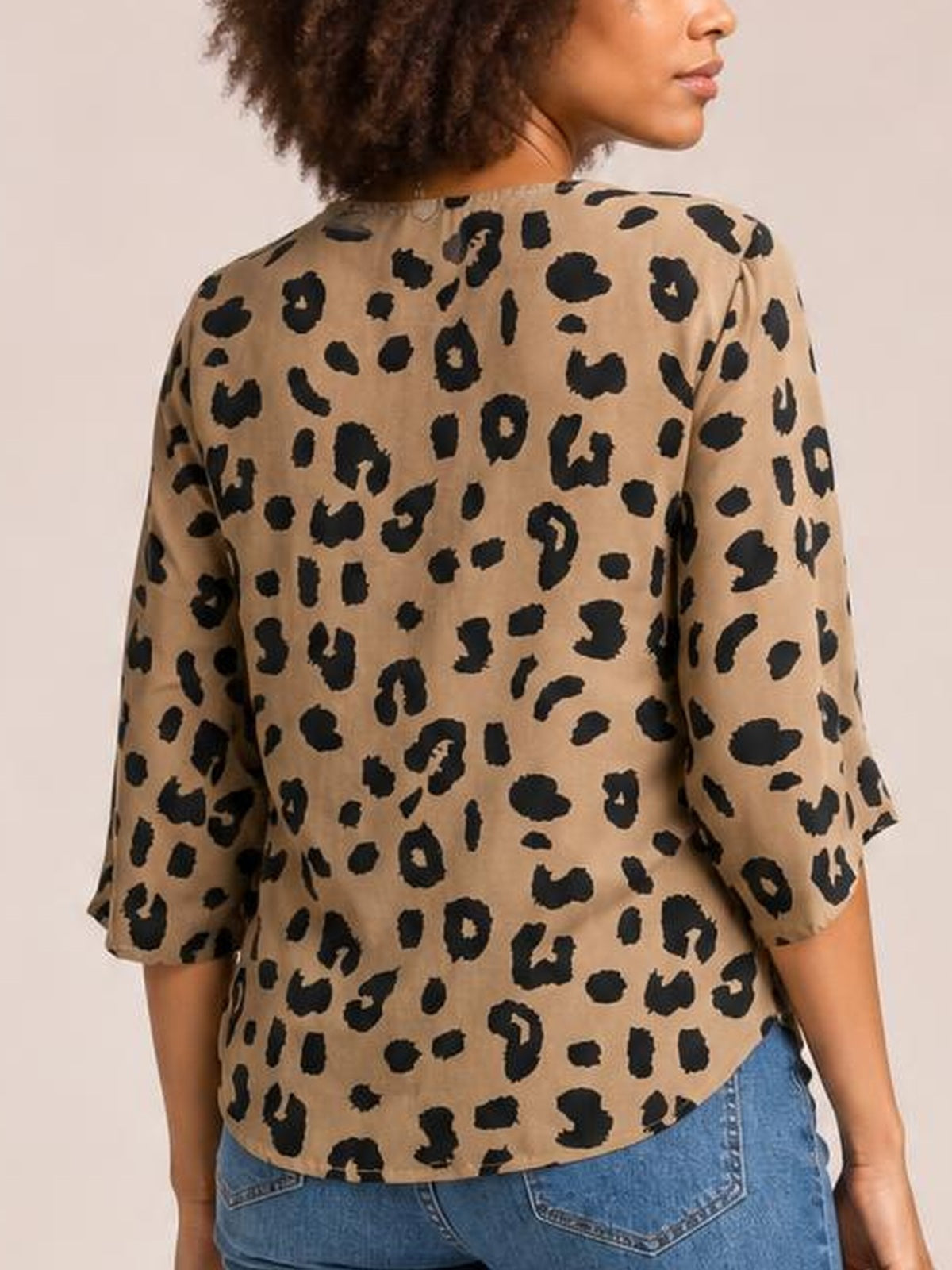 Model shown from behind wearing a tan leopard-print blouse with black spots, button front, three-quarter sleeves, relaxed silhouette, and curved hem.