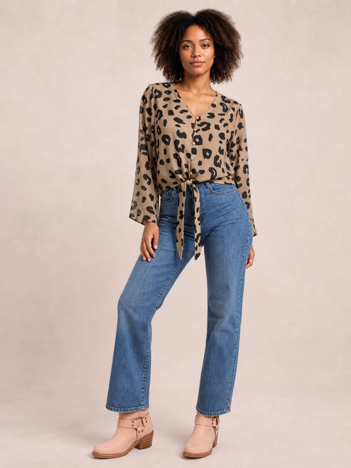 Model stands with one leg angled in a tan-and-black leopard-print V-neck blouse with a button front, long sleeves, and a tied waist for a relaxed silhouette.