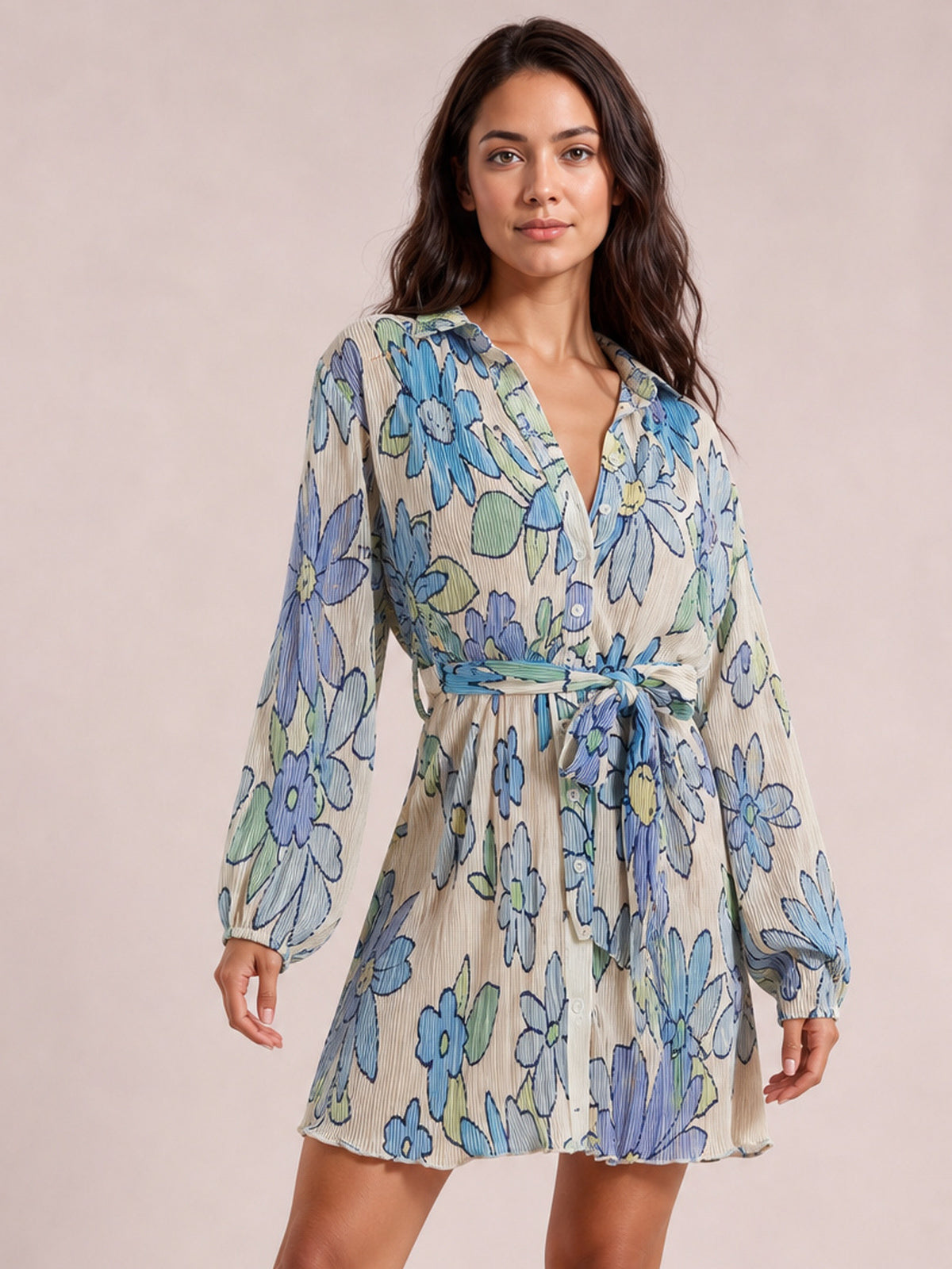 Model wearing a cream floral tied button-up dress with blue and green flowers, V-neckline, long sleeves, defined waist, and gently flared short silhouette.