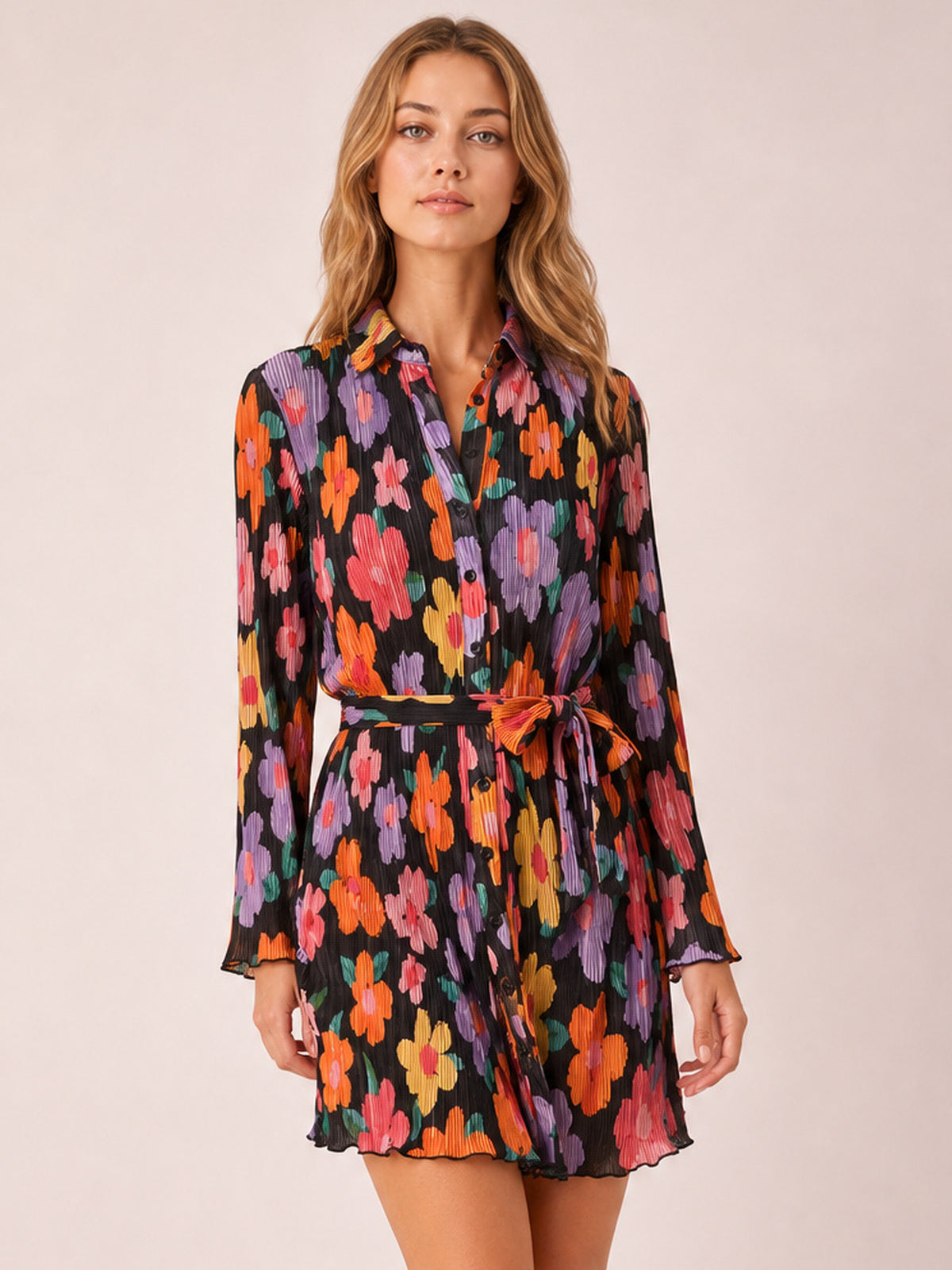 A model stands in a black floral tied button-up dress with a V-neckline, long sleeves, defined waist, and short flared silhouette.