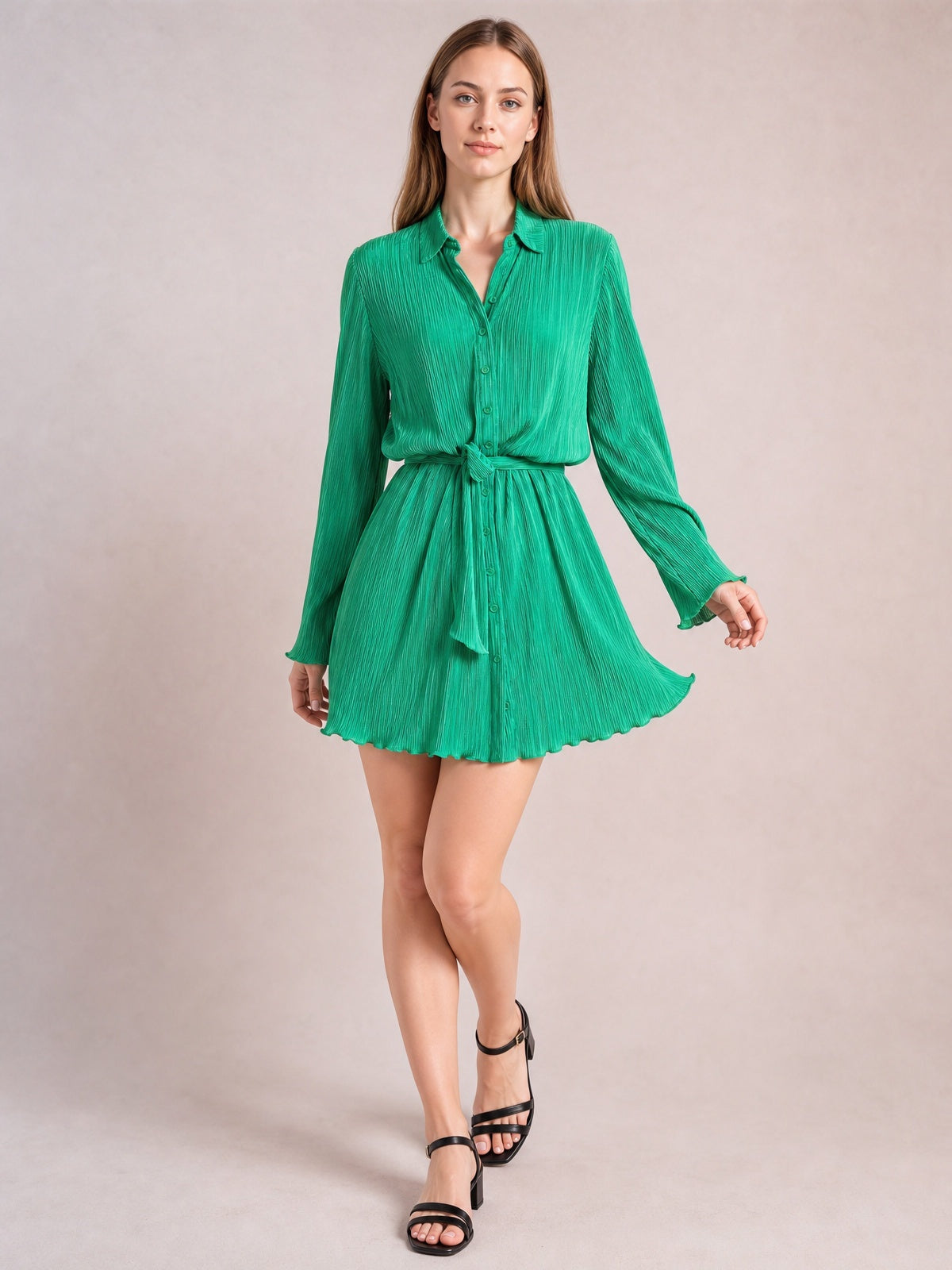 Model poses in a bright green tied button-up dress with a collared V-neck, long sleeves, defined waist, and gently flared short skirt.