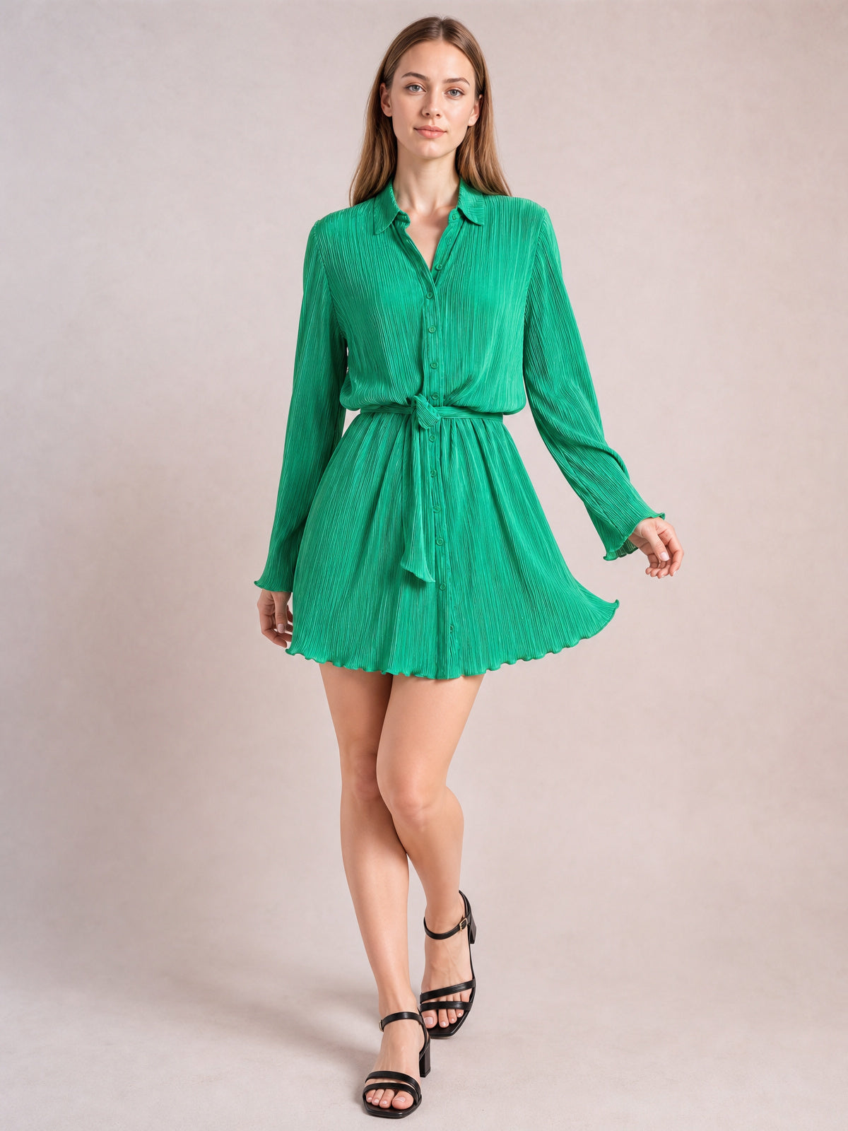 Model poses in a bright green tied button-up dress with a collared V-neck, long sleeves, defined waist, and gently flared short skirt.