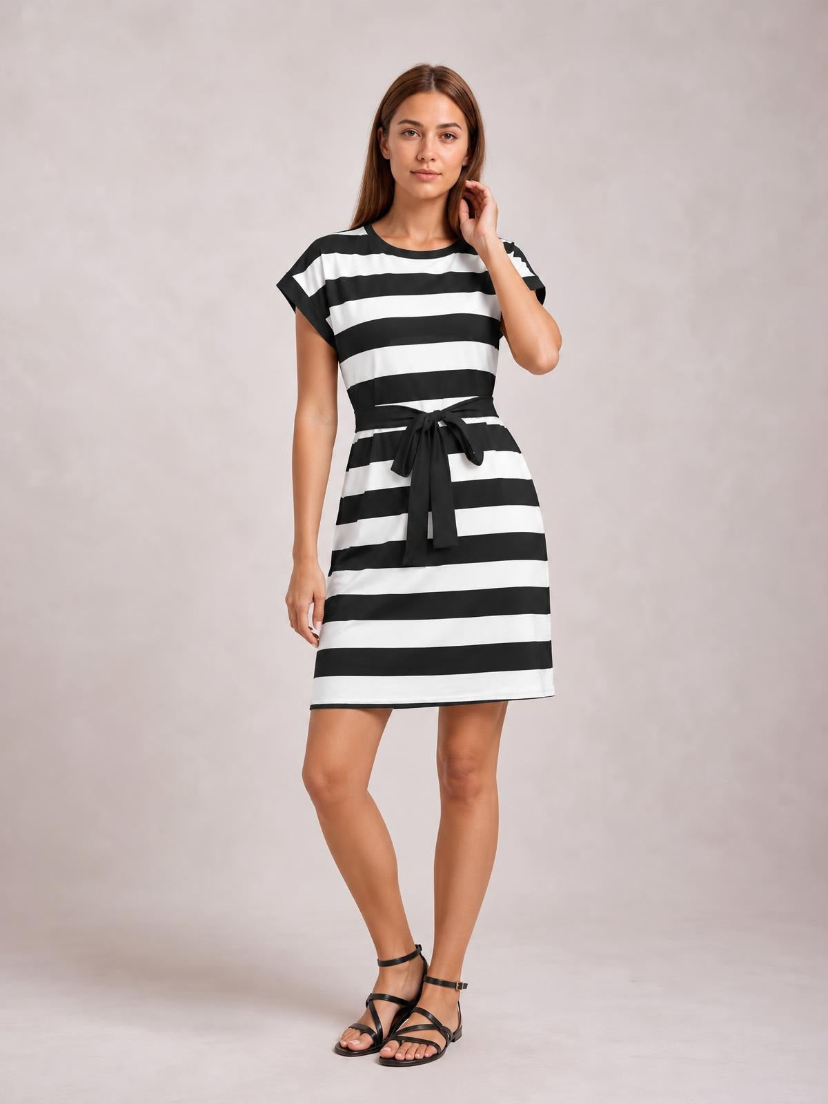 Model poses in a black-and-white contrast striped short sleeve mini tee dress with a crew neckline, straight silhouette, and tied waist.