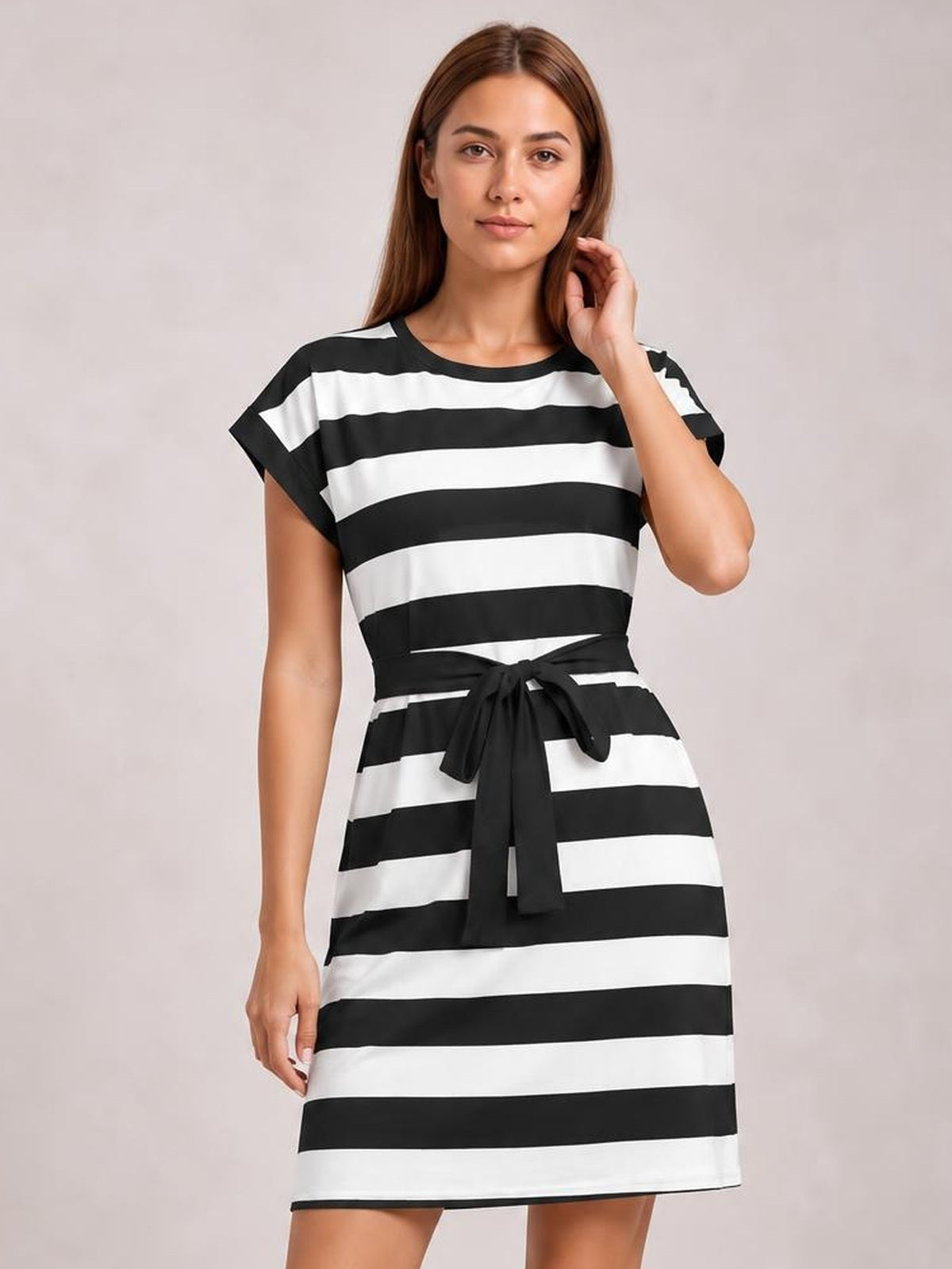 Model poses in a black-and-white contrast striped mini tee dress with short sleeves, a round neckline, straight silhouette, and tied waist.