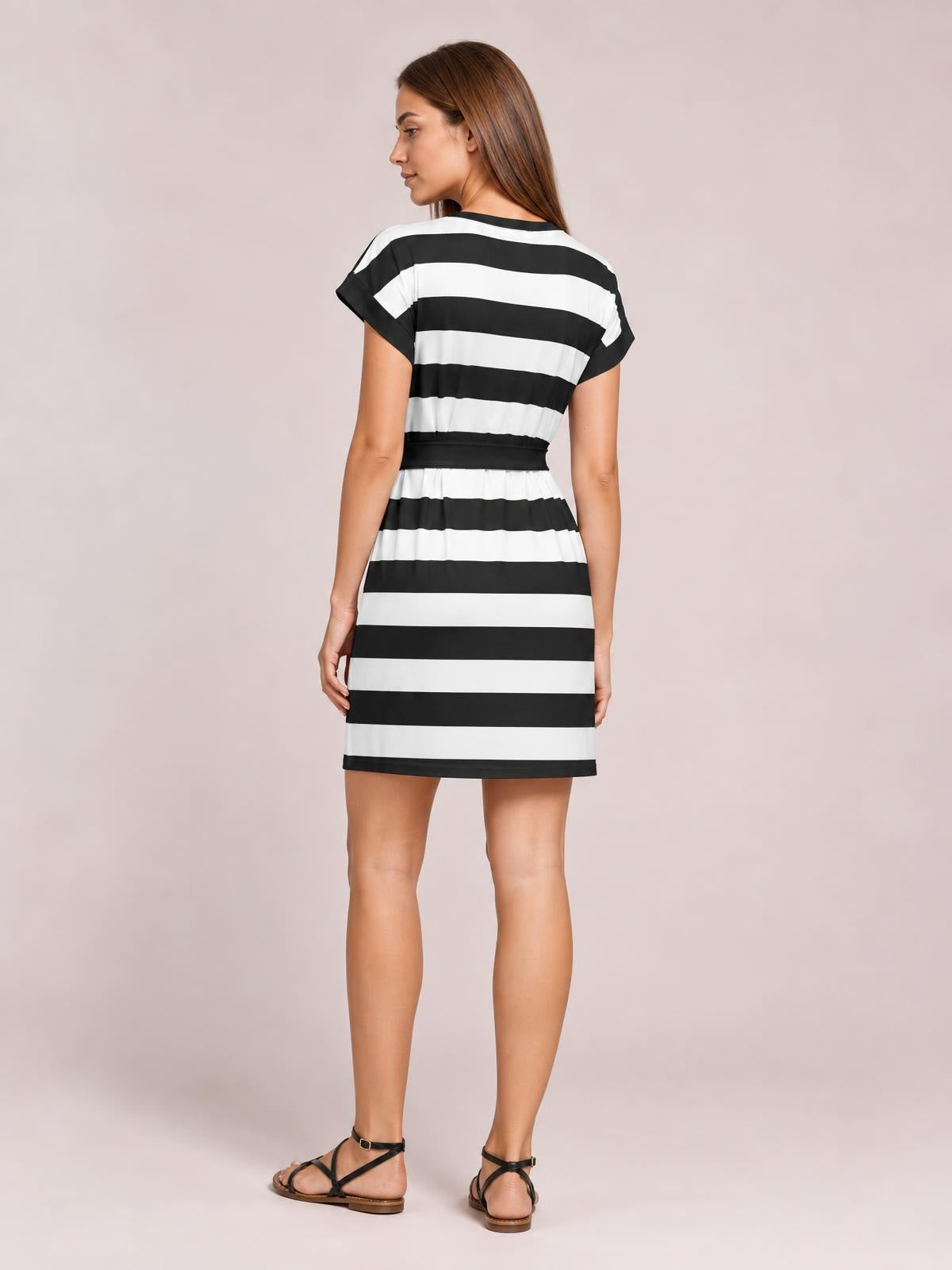 A model stands turned away in a black-and-white contrast striped mini tee dress with short cuffed sleeves, a black tied waist, and a straight above-knee silhouette.