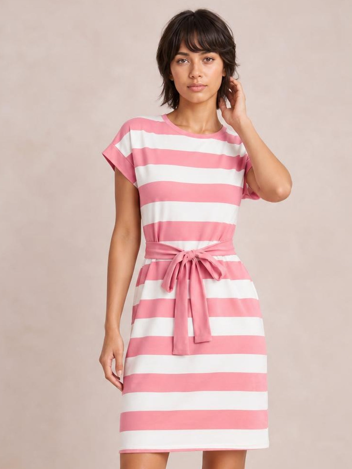 Model wearing a pink and white contrast striped short sleeve mini tee dress with a crew neckline, straight silhouette, and tied waist sash.