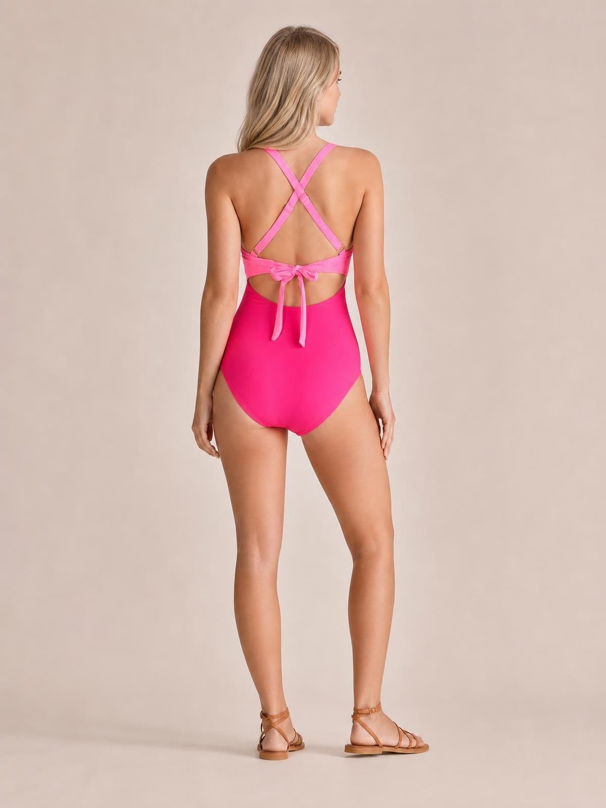 Model shown from behind in bright pink tied crisscross cutout one-piece swimwear with a stretchy fitted silhouette and open back.