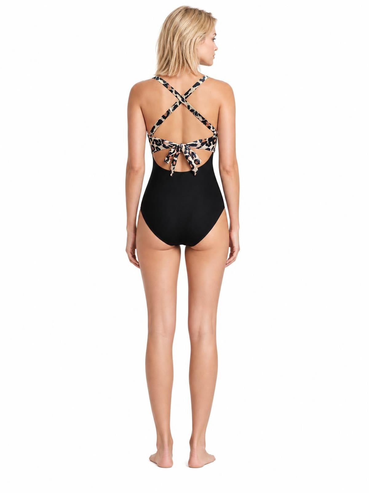Back view of a model in a black one-piece swimsuit with leopard-print crisscross straps, open-back cutout, and tied waist detail.
