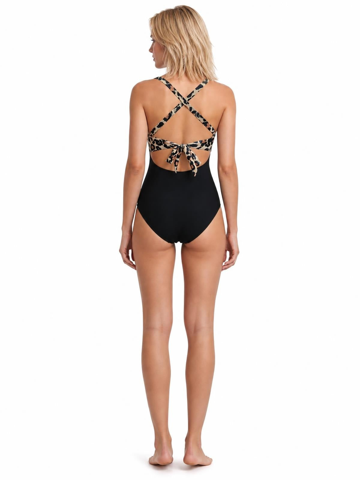 Model shown from behind wearing a black one-piece swimsuit with leopard-print crisscross straps, an open-back cutout, and a tied bow.