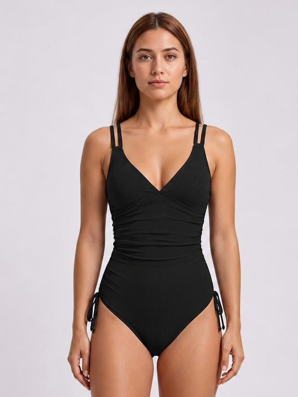Model standing in a black tied cutout one-piece swimsuit with a plunge neckline, double shoulder straps, ruched waist, and side ties.