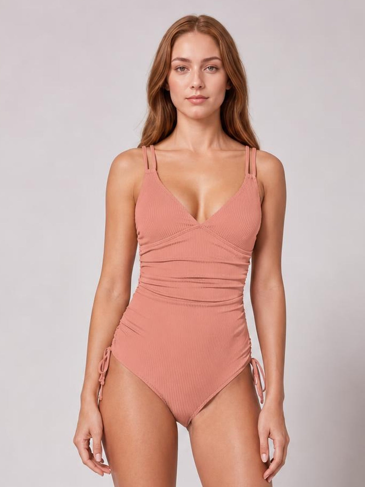 Front-facing model wears a dusty rose tied cutout one-piece swimsuit with a plunge neckline, double shoulder straps, ruched waist, and side-tie details.