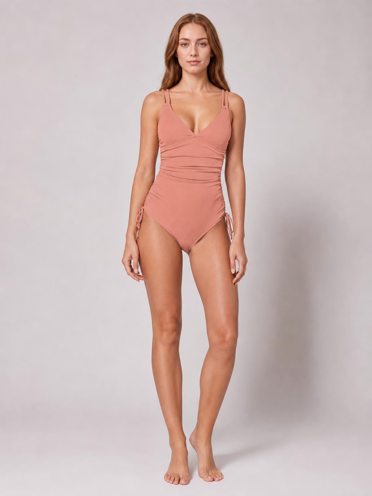 A model stands in a dusty rose tied cutout one-piece swimsuit with a plunge neckline, double straps, ruched waist, and side ties.